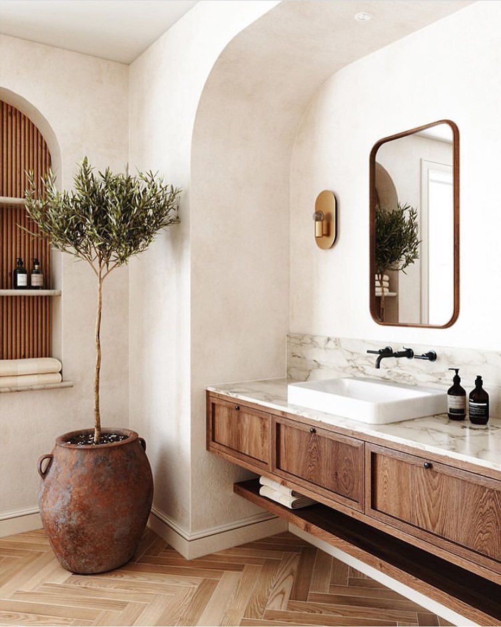 Warm oak bathroom vanity with marble top and brass mirror in an arched alcove